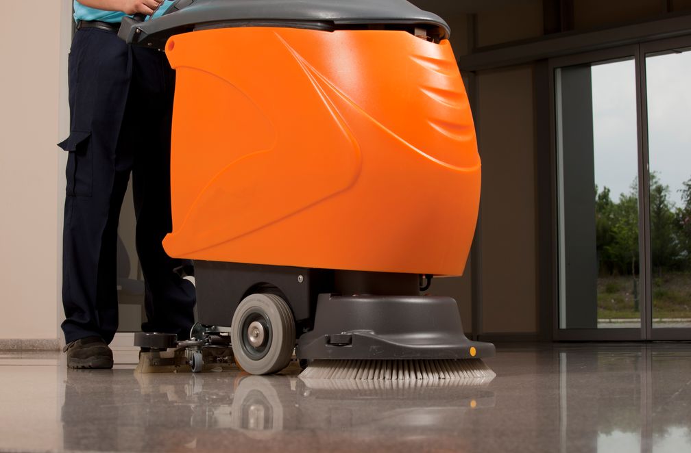 An individual utilizing a floor scrubber with orange and black color scheme for effective cleaning. An individual utilizing a floor scrubber with orange and black color scheme for effective cleaning.