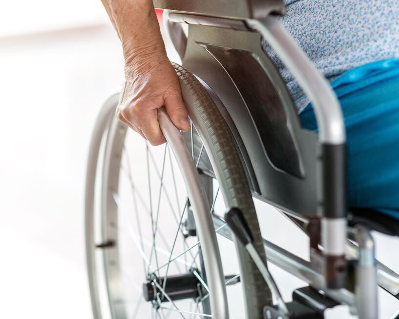 An individual in a wheelchair with their hand firmly grasping the wheel, showcasing mobility and self-reliance. An individual in a wheelchair with their hand firmly grasping the wheel, showcasing mobility and self-reliance.