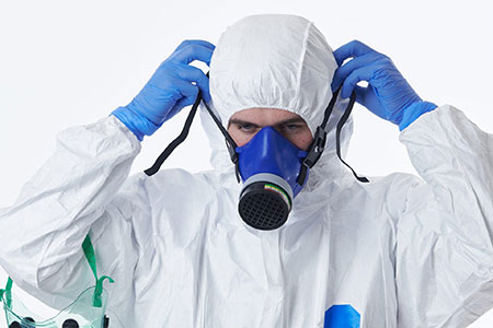 An individual in a protective suit and mask securely grasps a gas mask, demonstrating readiness for potential dangers.