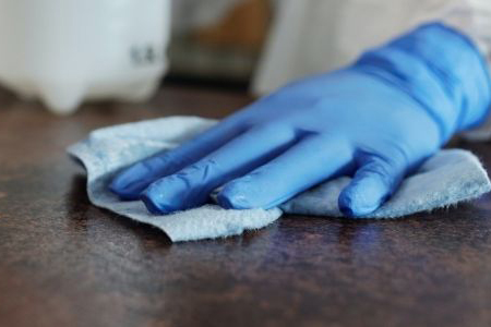 With utmost precision, a person in blue gloves diligently cleanses a table, leaving it immaculate and sanitized.