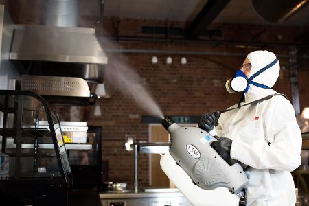 A person wearing a white suit skillfully operating a spraying machine, dispersing a substance with accuracy.