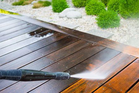 A person using a high-pressure water sprayer to thoroughly clean a wooden deck and restore its original appearance.