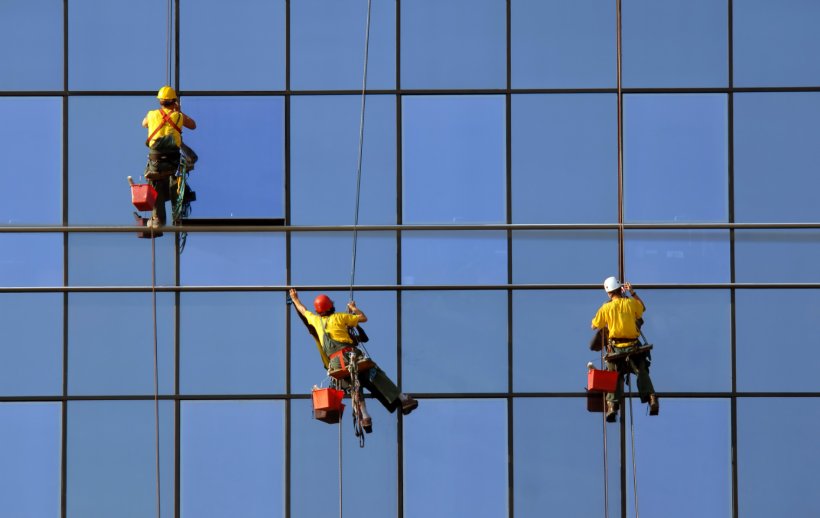 A team of four workers is seen cleaning the windows of a tall building, using squeegees and cleaning solution to ensure a spotless finish. A team of four workers is seen cleaning the windows of a tall building, using squeegees and cleaning solution to ensure a spotless finish.