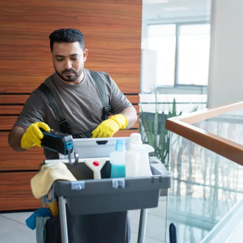 Professional janitor with cleaning cart performing commercial cleaning in an office building.
