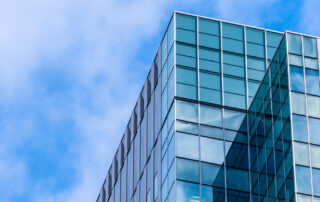 Modern glass office building with reflective windows under a bright blue sky, showcasing professional window cleaning results.